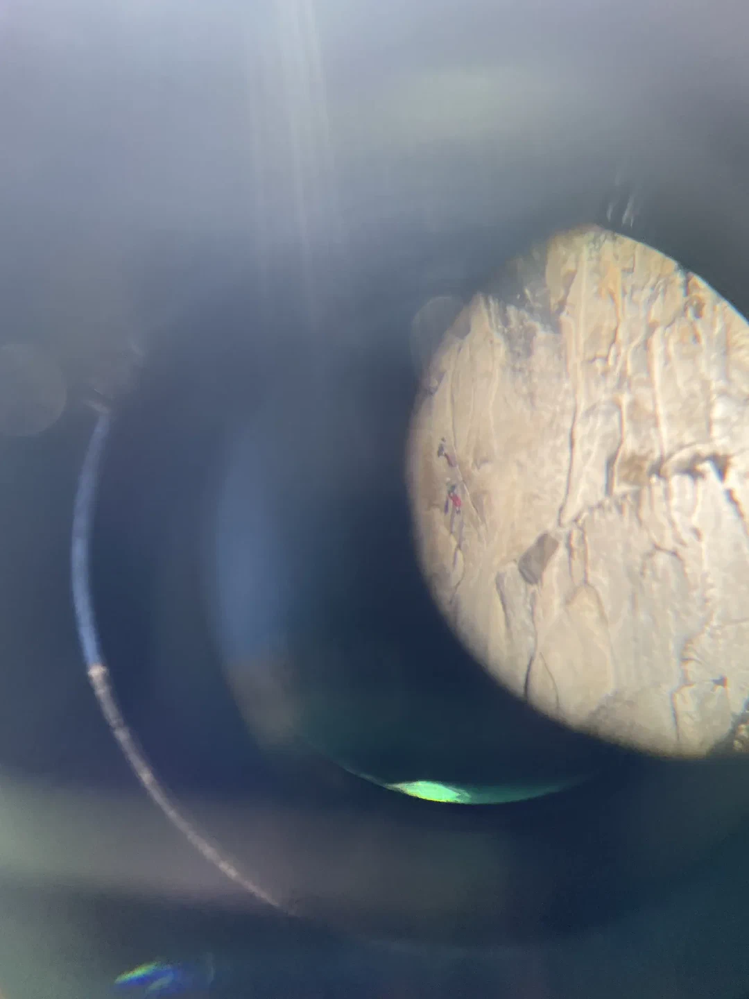 Climbers on a granite wall, seen through binoculars.