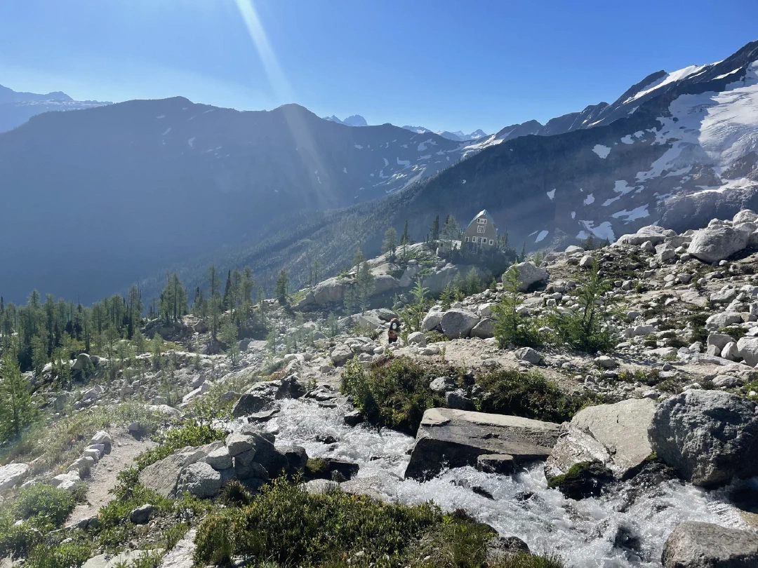 A creek tumbling across the trail, the Conrad Kain Hut on a bluff in the valley below