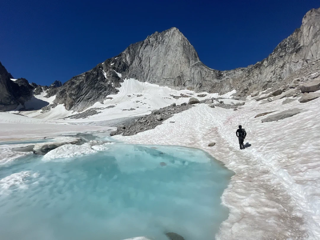 A climber skirting a turquoise melt pool on the glacier beneath Bugaboo Spire.
