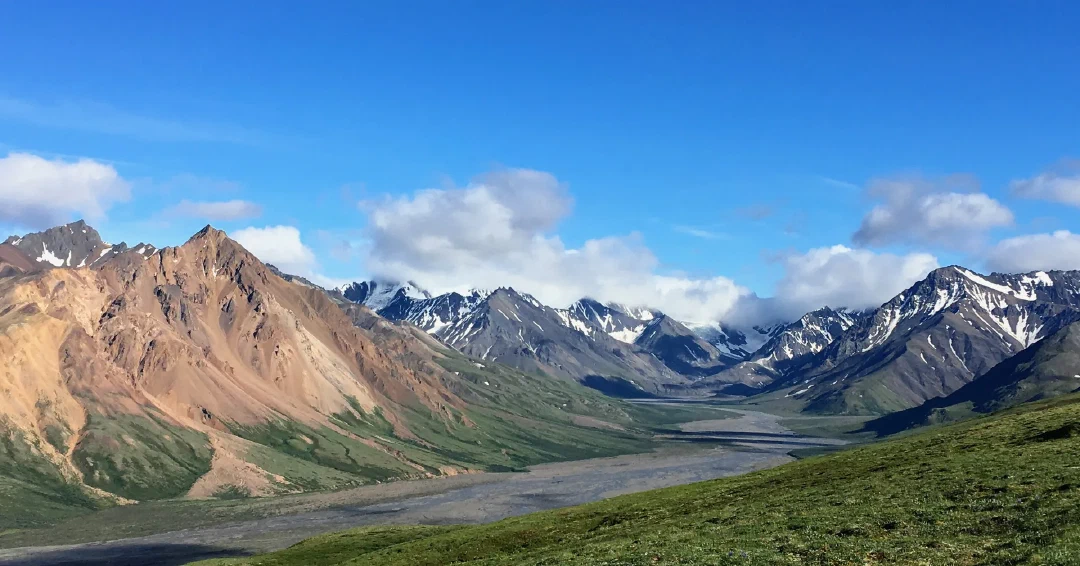 Rust-and-green ridge transitioning to snow-streaked peaks under a bright blue sky.