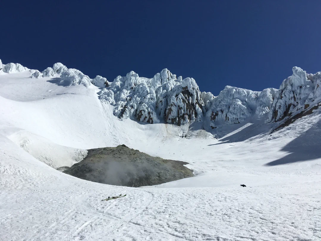 Rime-crusted crater rim, steam rising from the fumaroles of Devil's Kitchen. A solo climber traverses the Hogsback and a few more navigate left chute of the Pearly Gates high above.