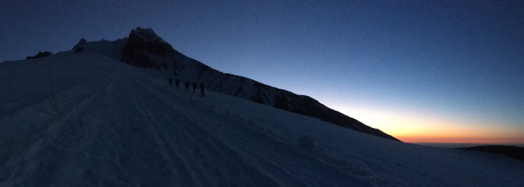 A rope team silhouetted on the snowfield at first light.