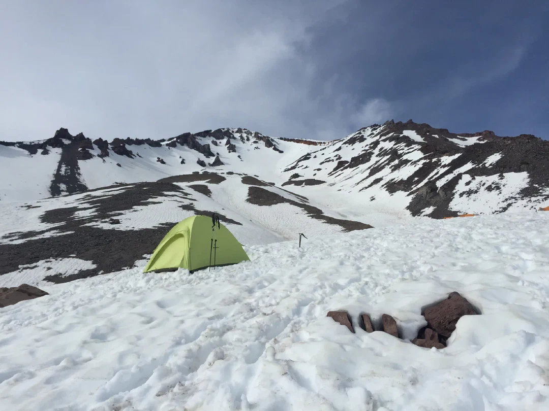 A green tent dug into the snow at high camp, the summit ridge rising behind