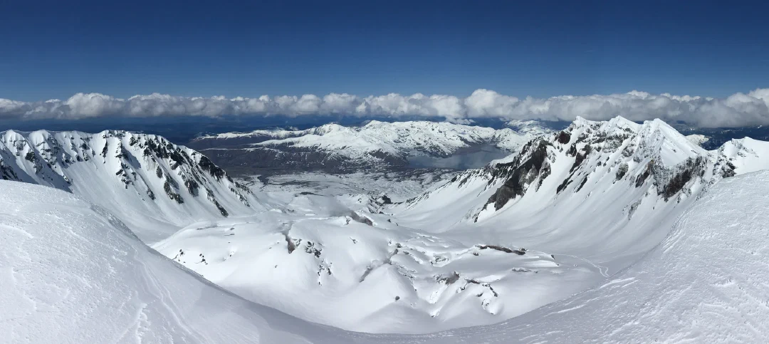 Looking into the snow-filled crater from the rim, Spirit Lake and blast-zone ridges beyond