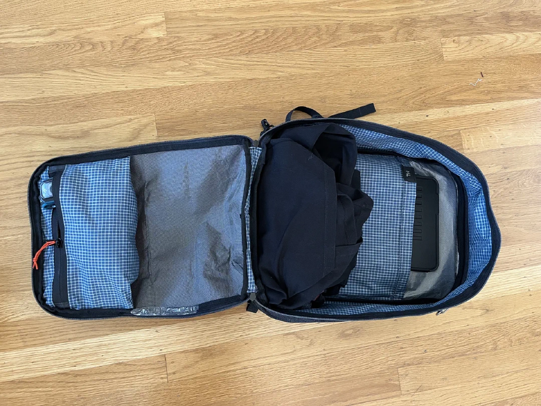 The finished pack unzipped flat clamshell-style, packed with a midlayer, iPad, and a headlamp in zipped pocket.